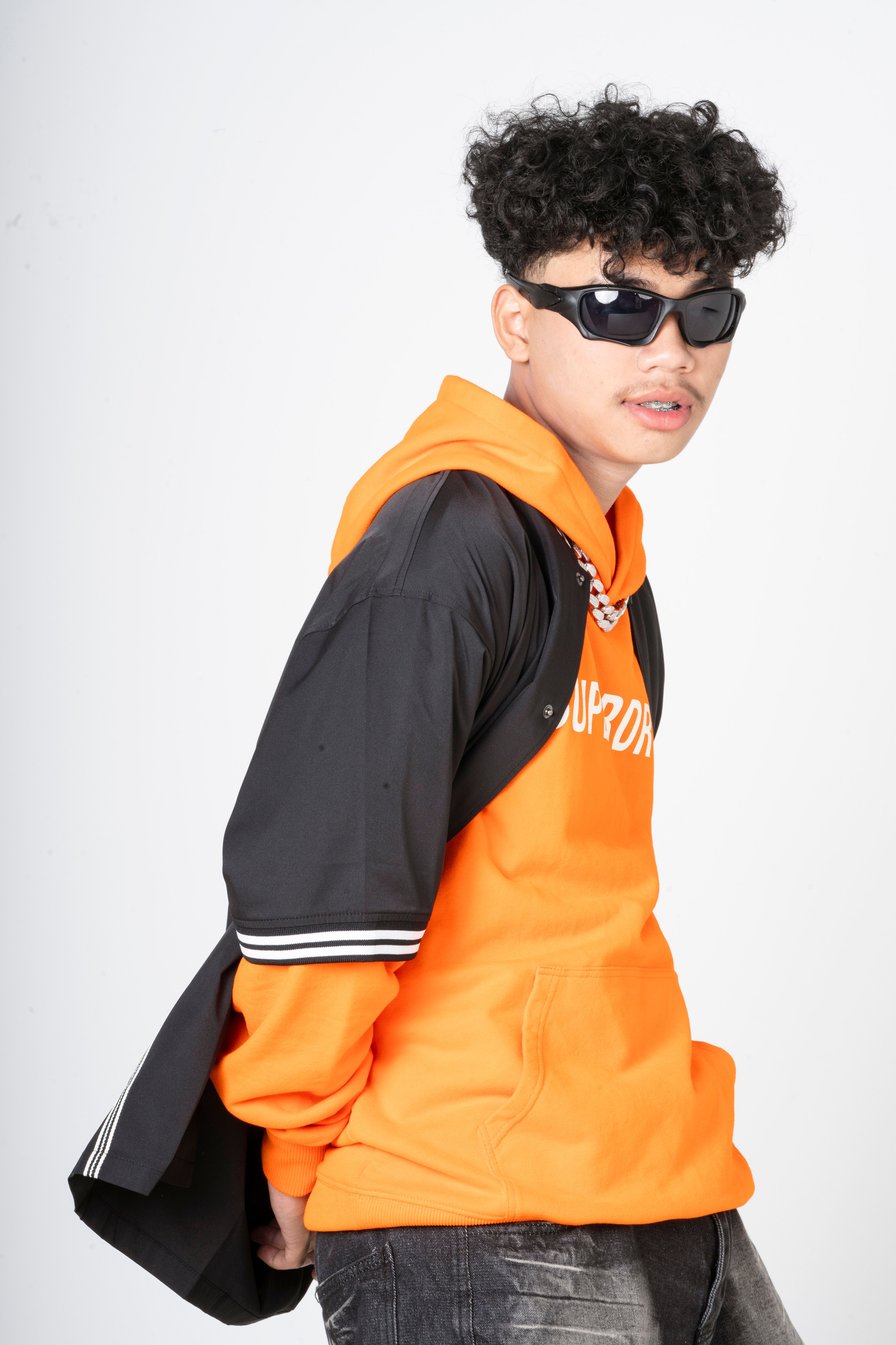 Stylish young adult in orange hoodie and shades, modern fashion portrait.