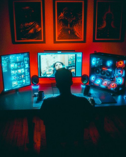 бесплатная Геймер, увлеченный яркой RGB-подсветкой на компьютере с двумя мониторами ночью. Стоковое фото