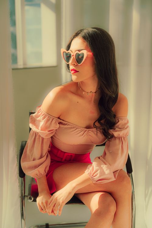 Free A fashionable woman wearing heart-shaped sunglasses sits elegantly in natural light, exuding a chic and relaxed vibe. Stock Photo