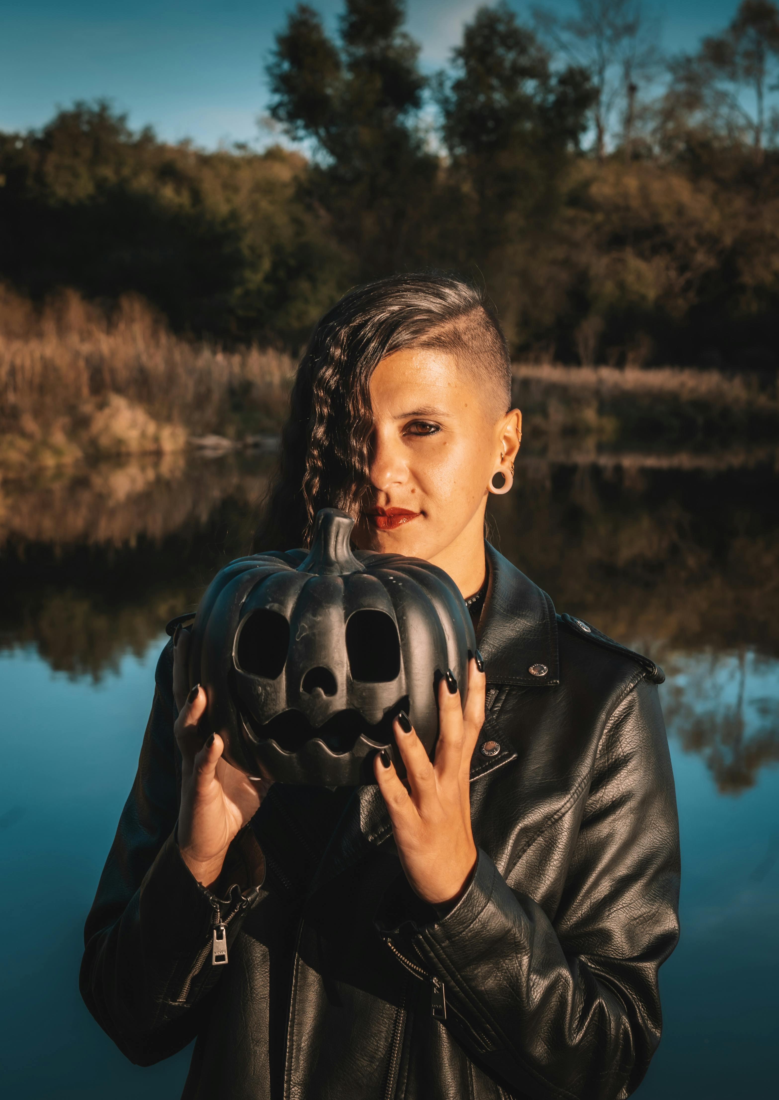 Person holding a black pumpkin near a serene lake, creating a mysterious, Halloween vibe.