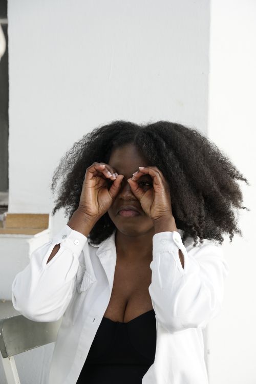 Free An adult woman playfully uses her hands to mimic binoculars while sitting indoors. Stock Photo