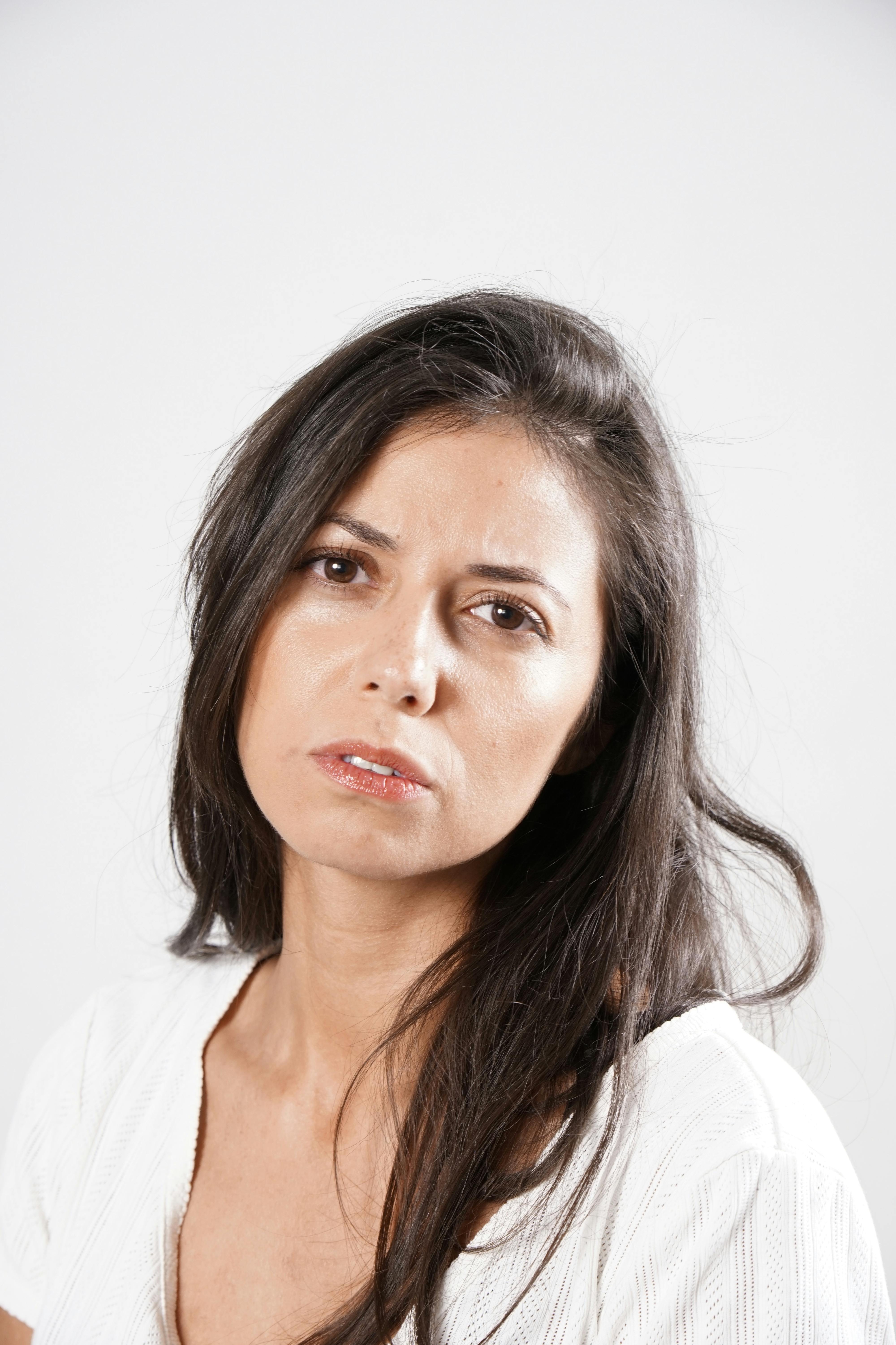 Kostenlos Nahaufnahme einer nachdenklichen erwachsenen Frau in einem weißen Oberteil vor einem neutralen Hintergrund. Stock-Foto