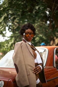 Fashionable woman in sunglasses posing confidently by a vintage car outdoors.