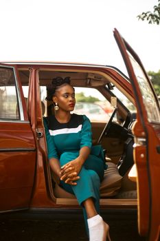Stylish woman in a teal dress sitting in a vintage brown car outdoors.