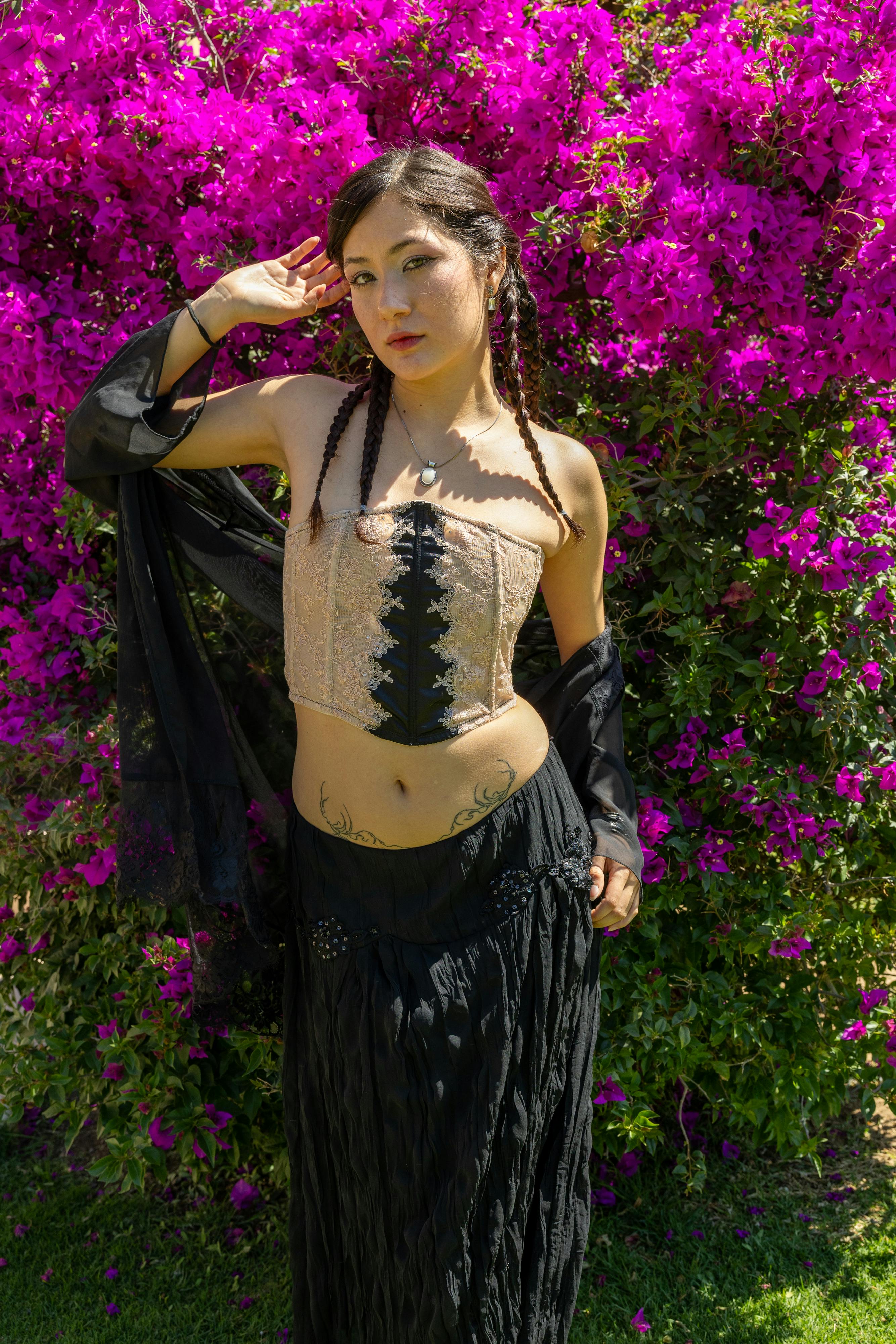 Free A young woman poses in a bohemian outfit against a vibrant floral backdrop in bright daylight. Stock Photo
