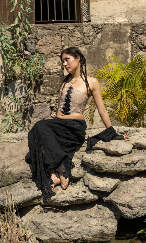 Free Woman in stylish outfit seated on rocks in a sunny outdoor setting, surrounded by foliage. Stock Photo