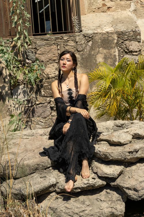 Free A woman in a black dress sits elegantly on stone steps against a rustic backdrop. Stock Photo