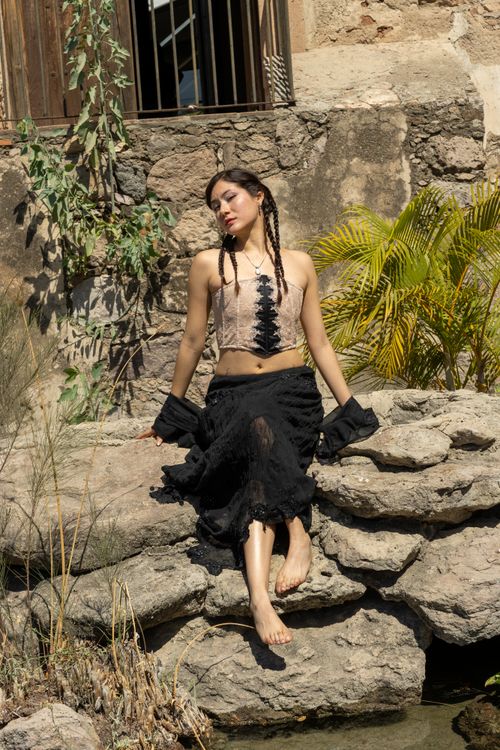 Free A woman poses in bohemian clothing on rocks by a rustic wall, exuding a carefree vibe. Stock Photo