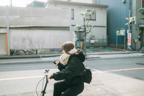 Free A woman cycling in a Japanese city street, wearing winter clothing. Stock Photo