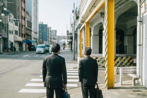 Free Two businessmen in suits crossing a street in an urban Japanese setting, reflecting daily city life. Stock Photo