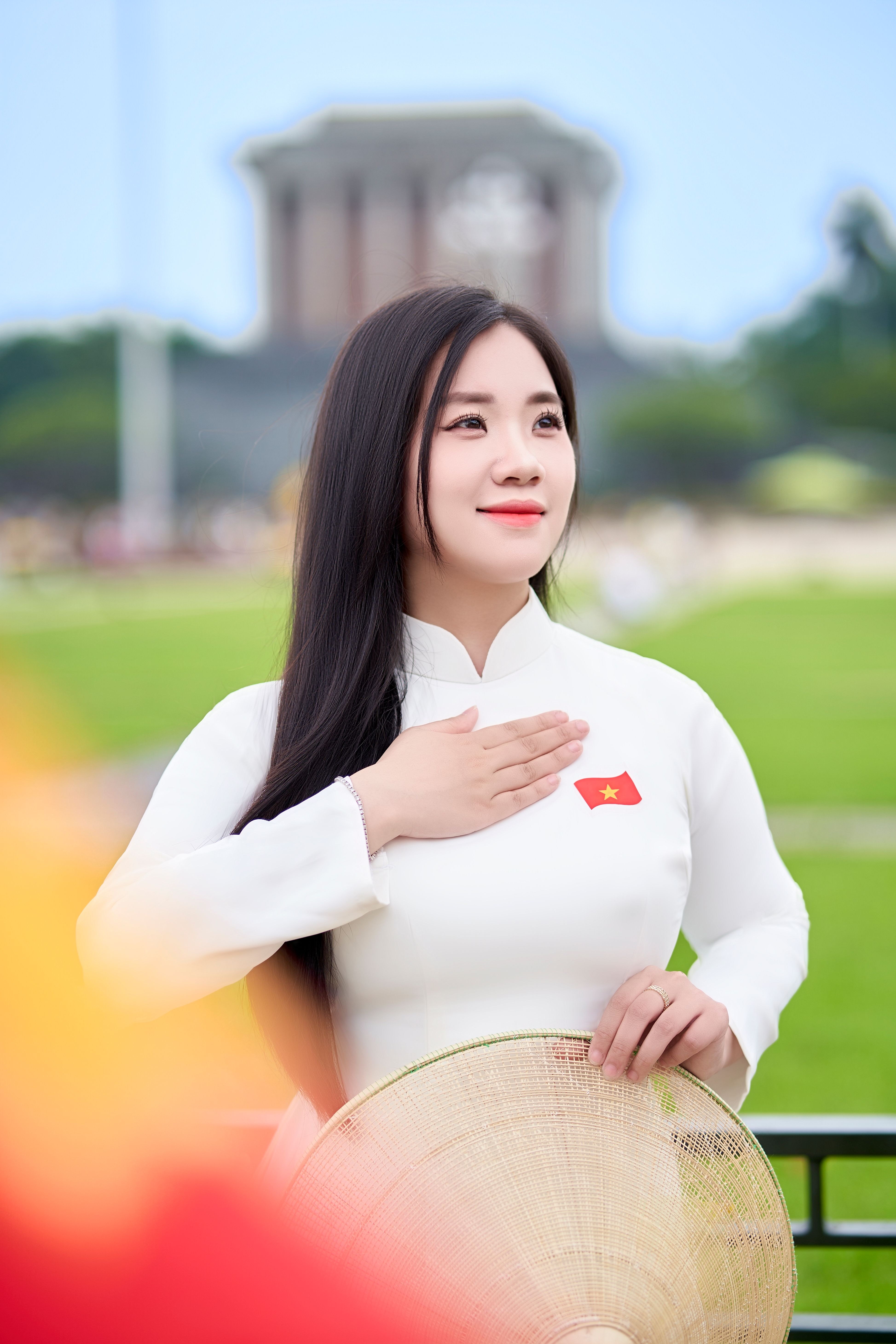 Elegant Vietnamese woman in a white Ao Dai, standing outdoors with a cultural landmark in the background.