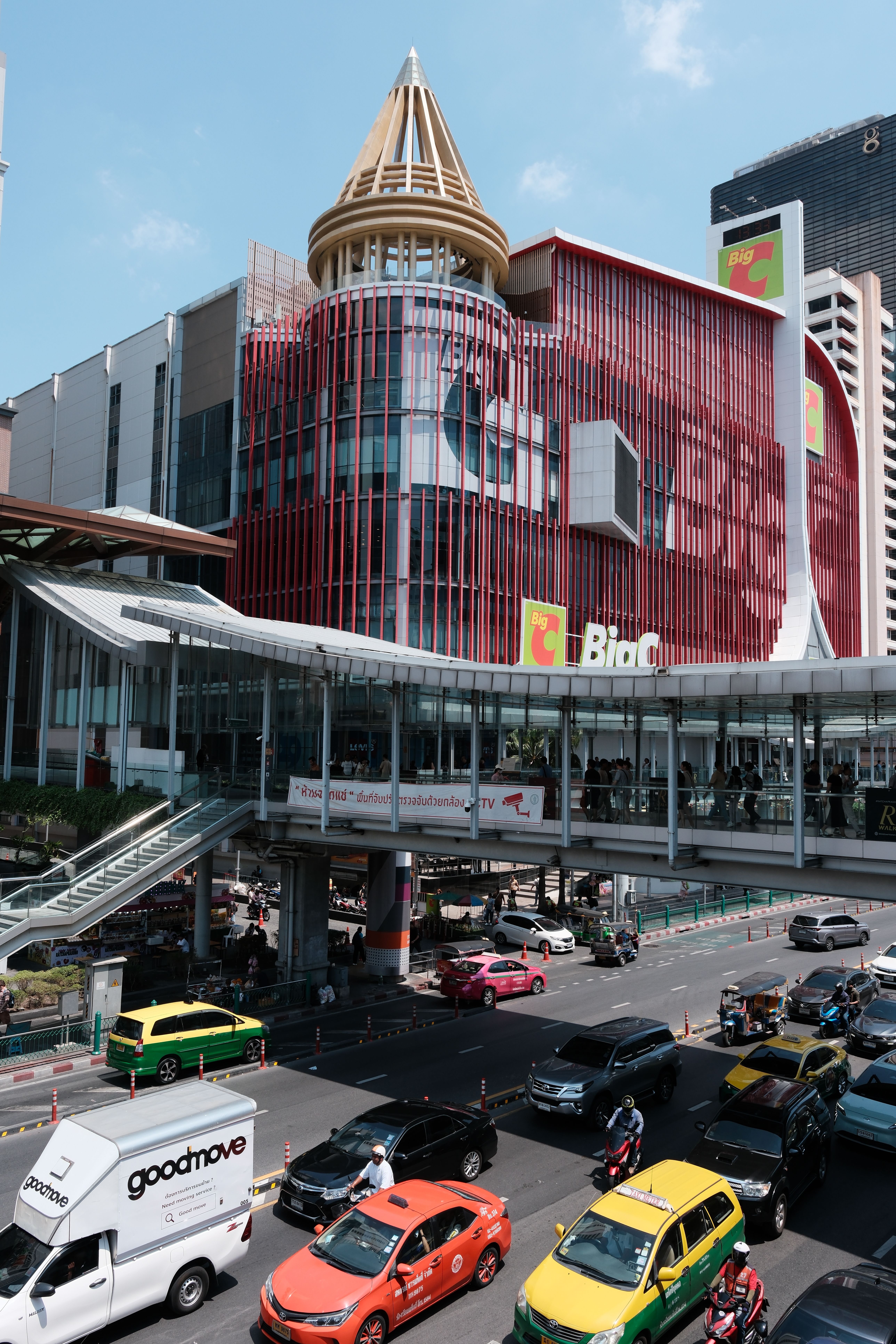 Urban cityscape featuring busy traffic and modern shopping mall architecture under a clear blue sky.