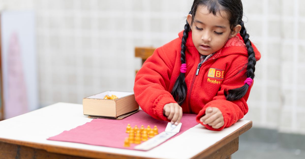 Une jeune fille sud-asiatique portant une veste rouge se concentre sur une tâche d’apprentissage à l’école.