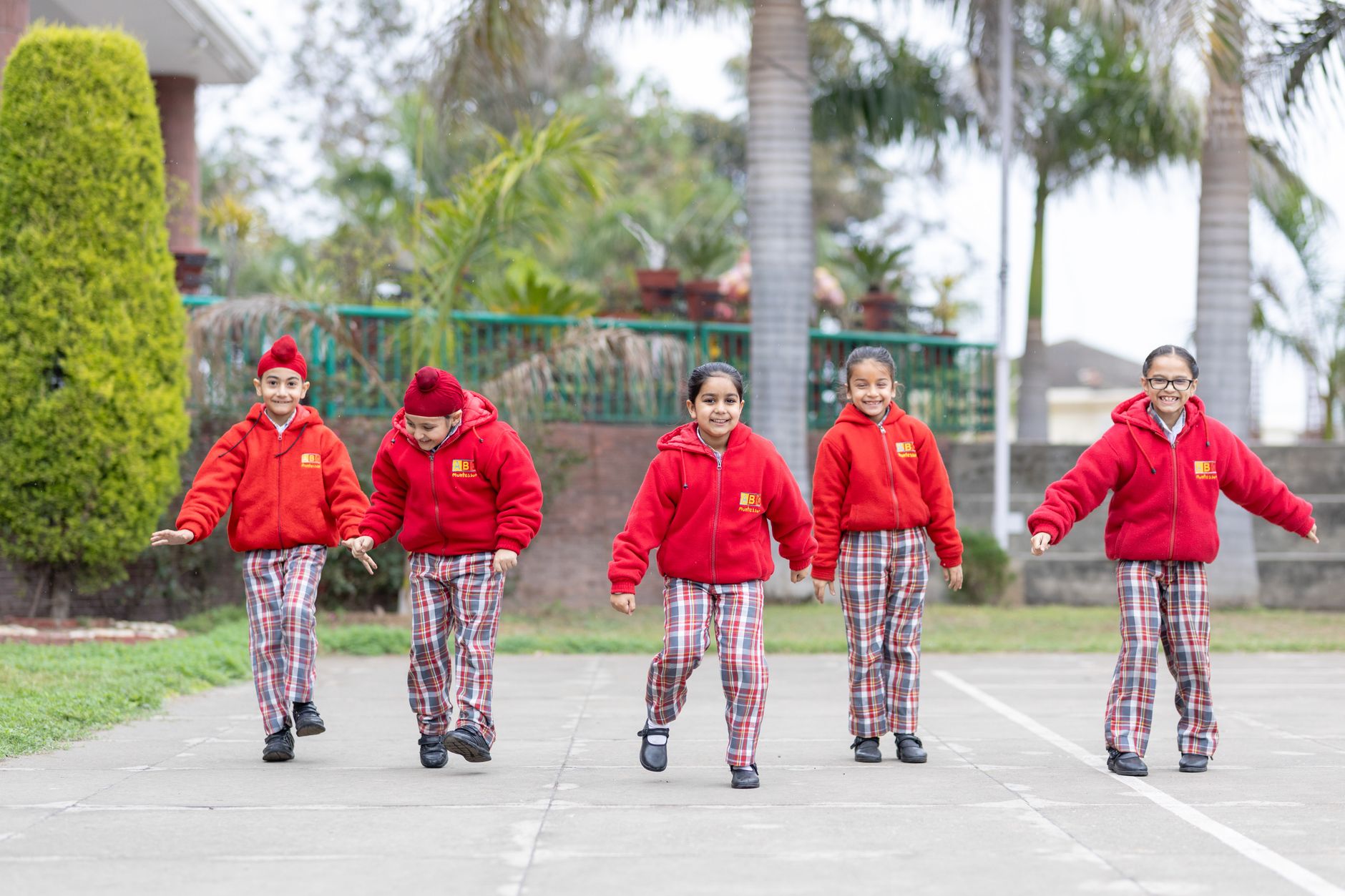 Group of schoolchildren in matching red uniforms smiling outdoors.
