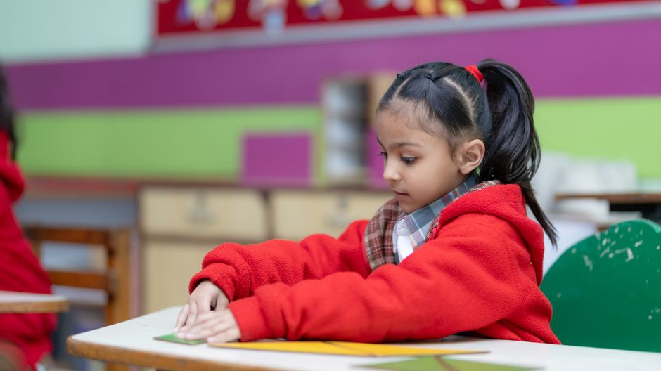 A young girl focusing intently on a classroom activity at her desk.