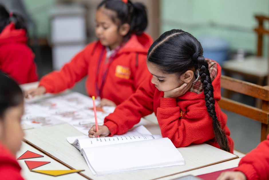 Children in red uniforms focused on writing exercises at school desk.