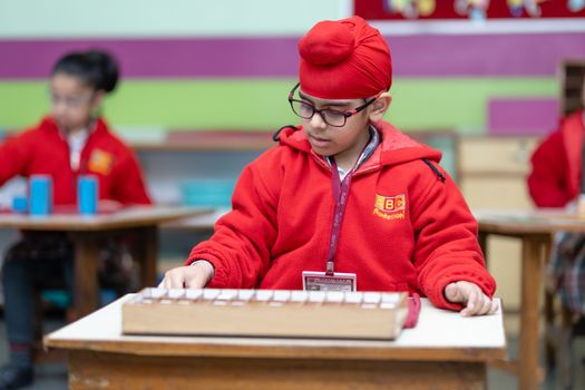 A child in a Montessori school setting focusing on an educational task, wearing a red turban and jacket. — photo by Bhupindra International Public School