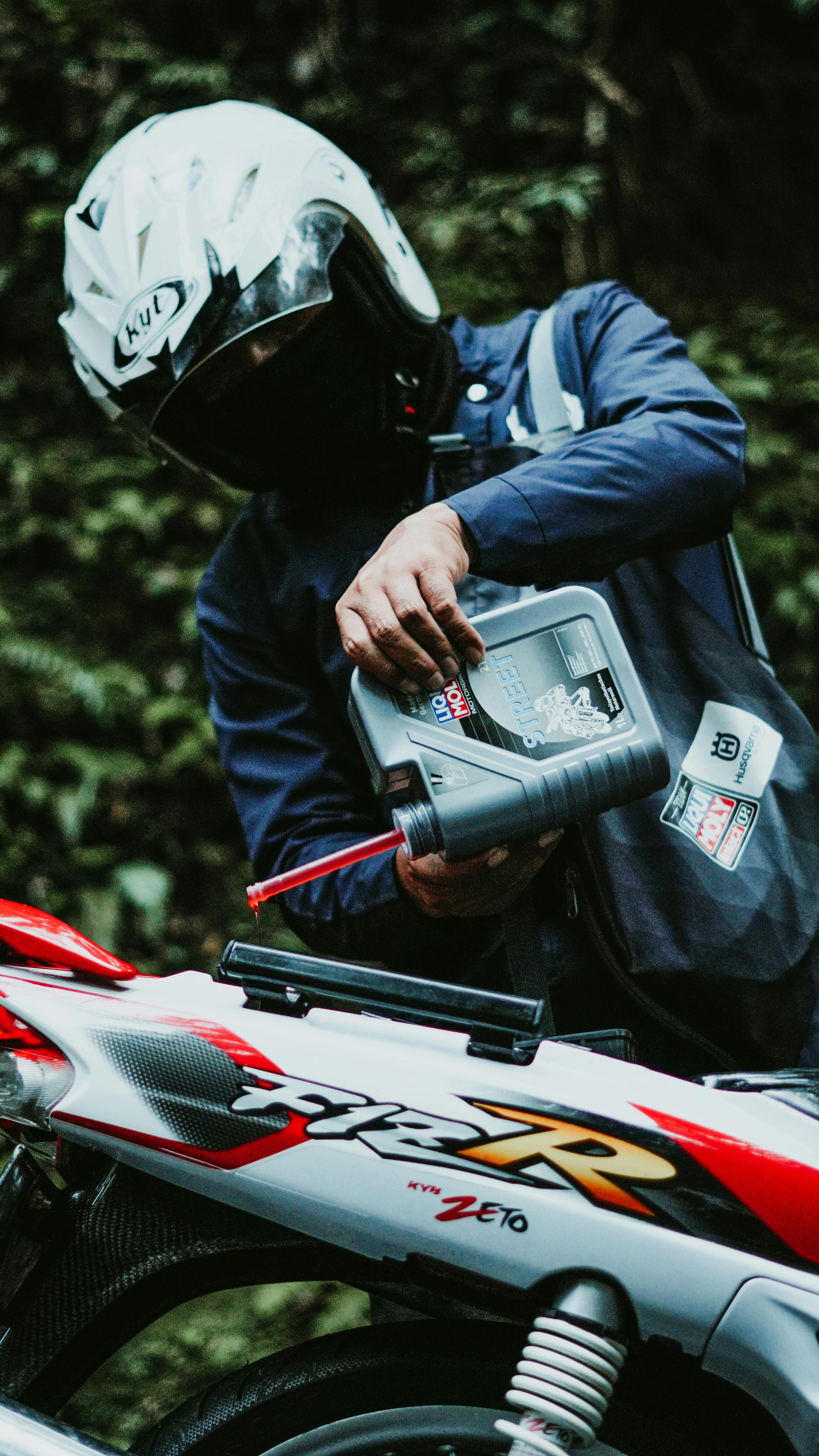 A person in motorcycle gear pouring engine oil into a motorbike in Jakarta, Indonesia.