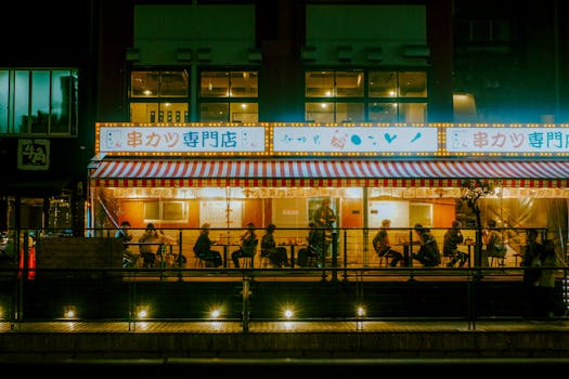 Candid street view of a bustling Japanese eatery in Osaka's Dotonbori at night, showcasing vibrant neon lights and urban life.