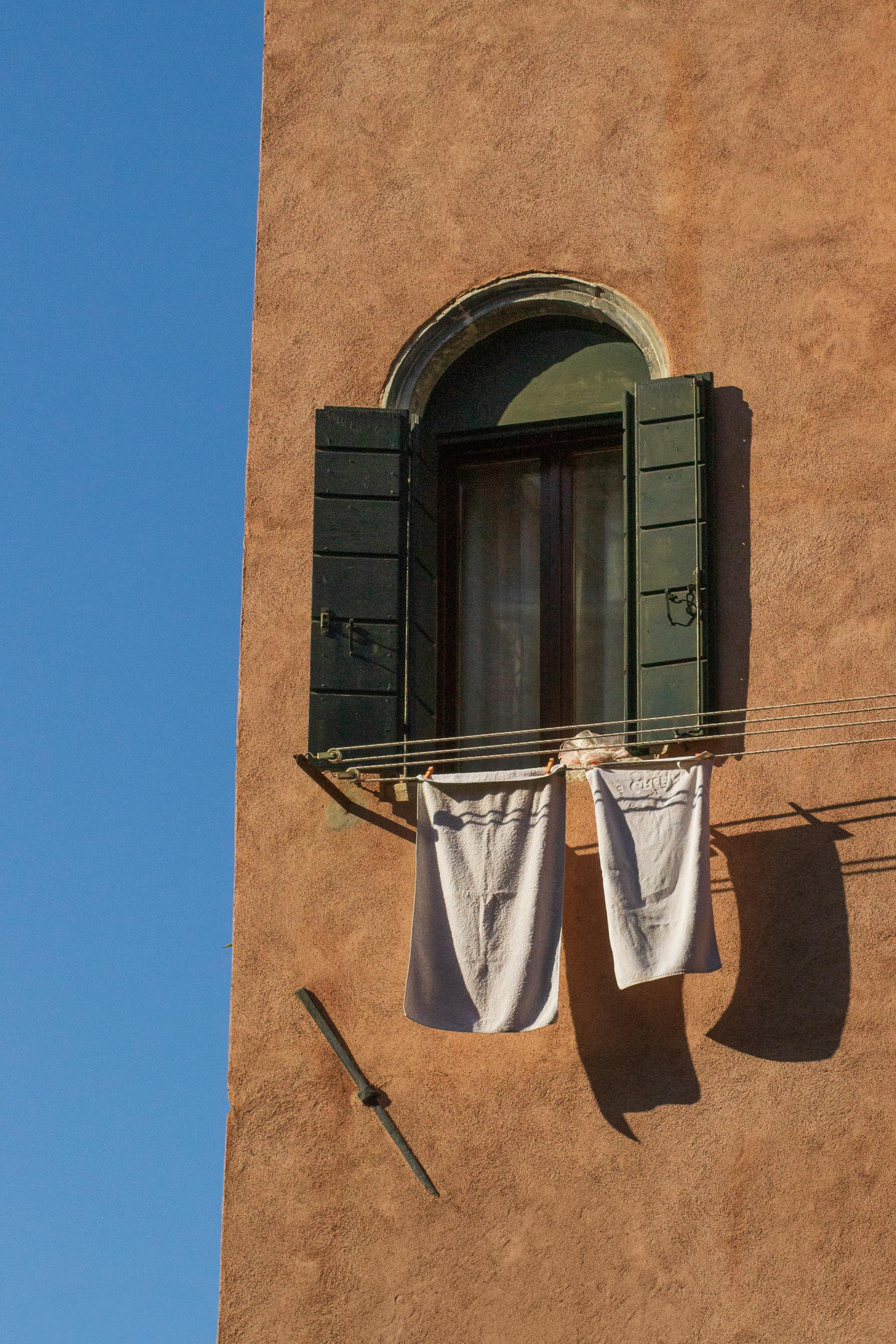 Sunlit window with shutters and laundry in Venice, Italy.