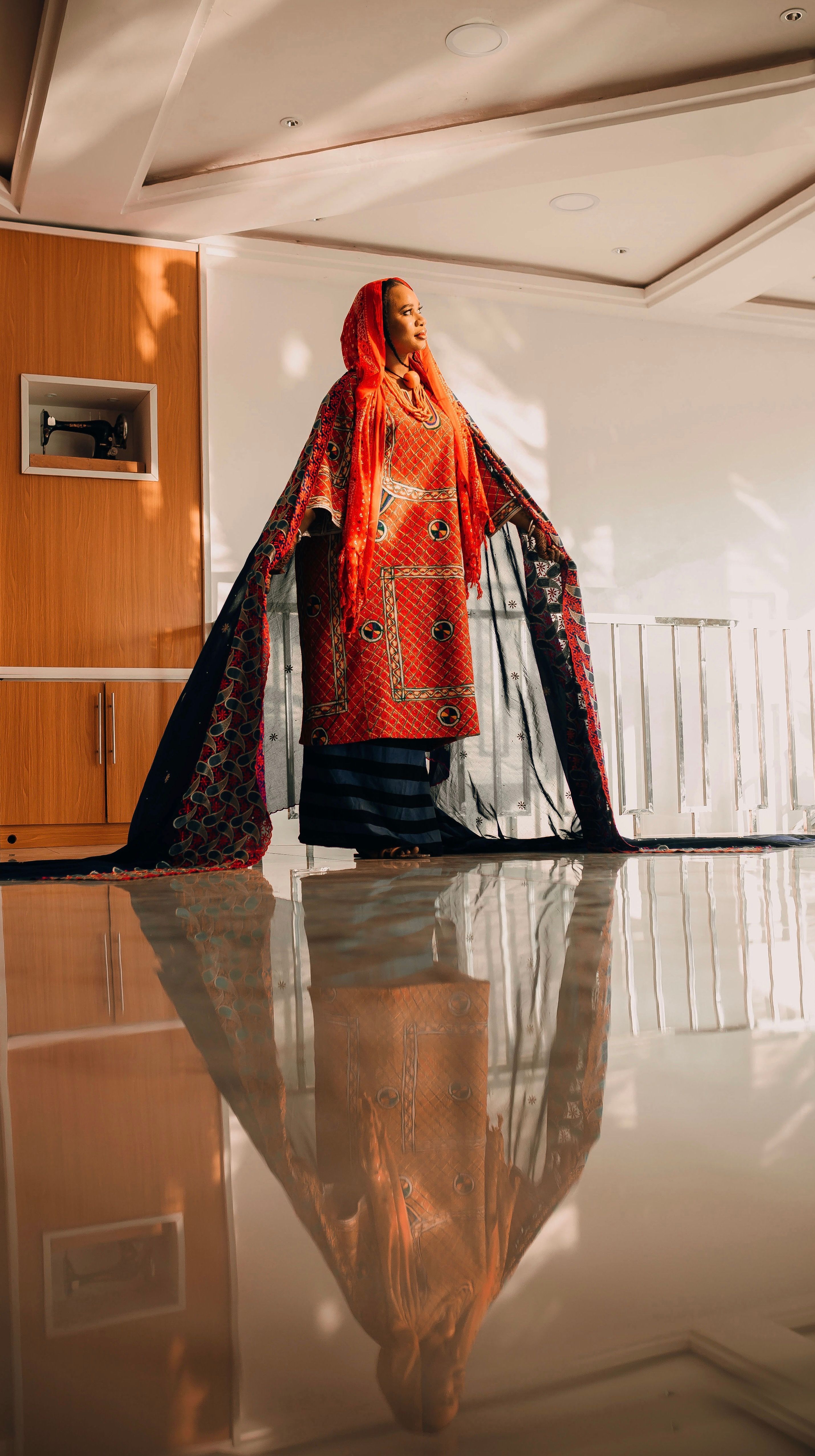 Woman in vibrant traditional clothing with reflection indoors.