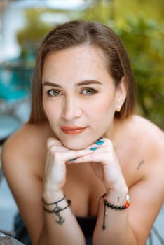 Charming portrait of a woman smiling outdoors with hands under chin, capturing a serene expression.