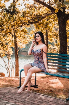 阳光明媚的公园里，一名身穿花卉连衣裙的年轻女子坐在长凳上，周围树木环绕