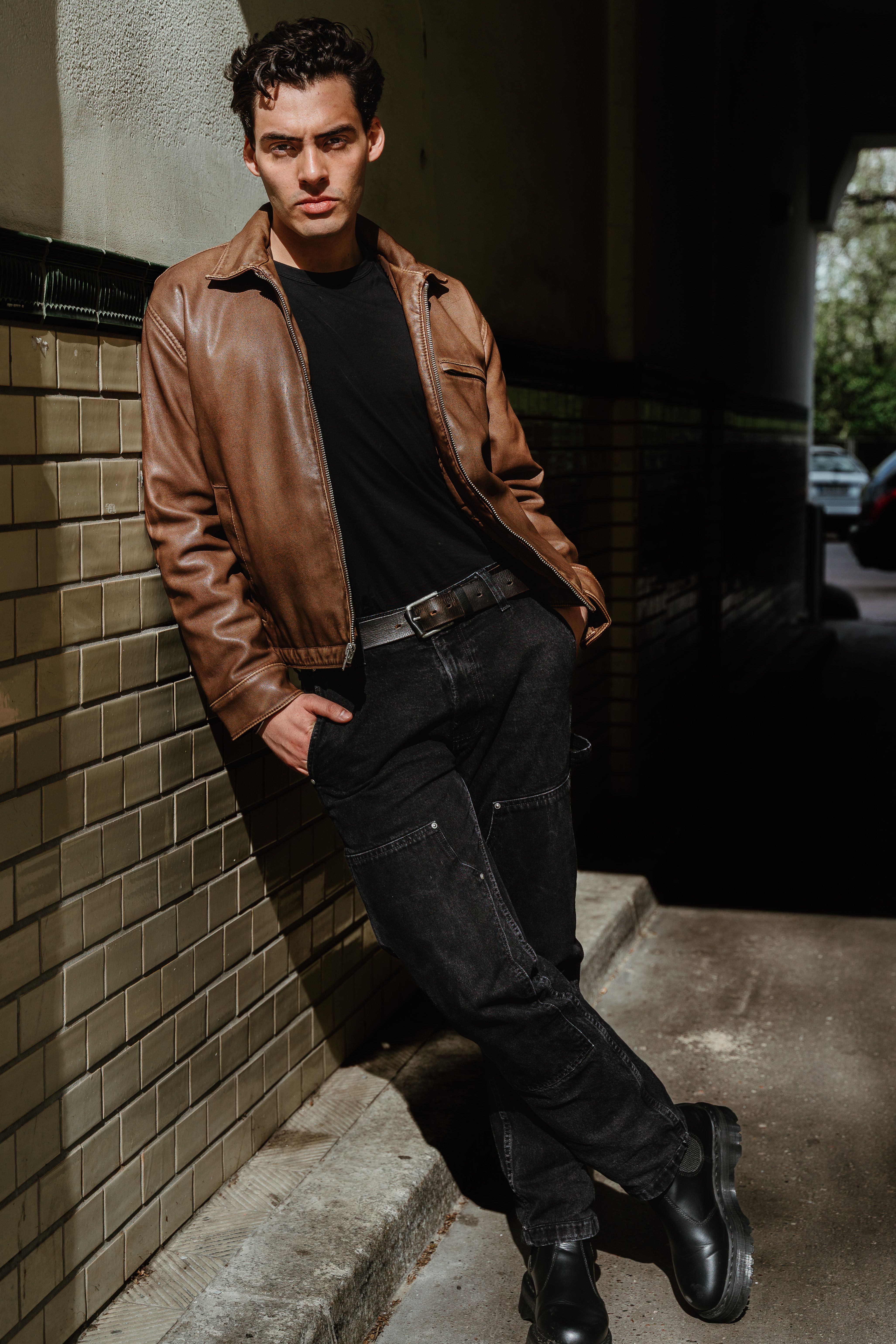 Confident male model in casual attire standing in a sunlit alley in Berlin, showcasing modern style.