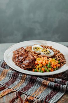 Grilled pork chop with seasoned quinoa and fresh vegetables on a stylish plate.