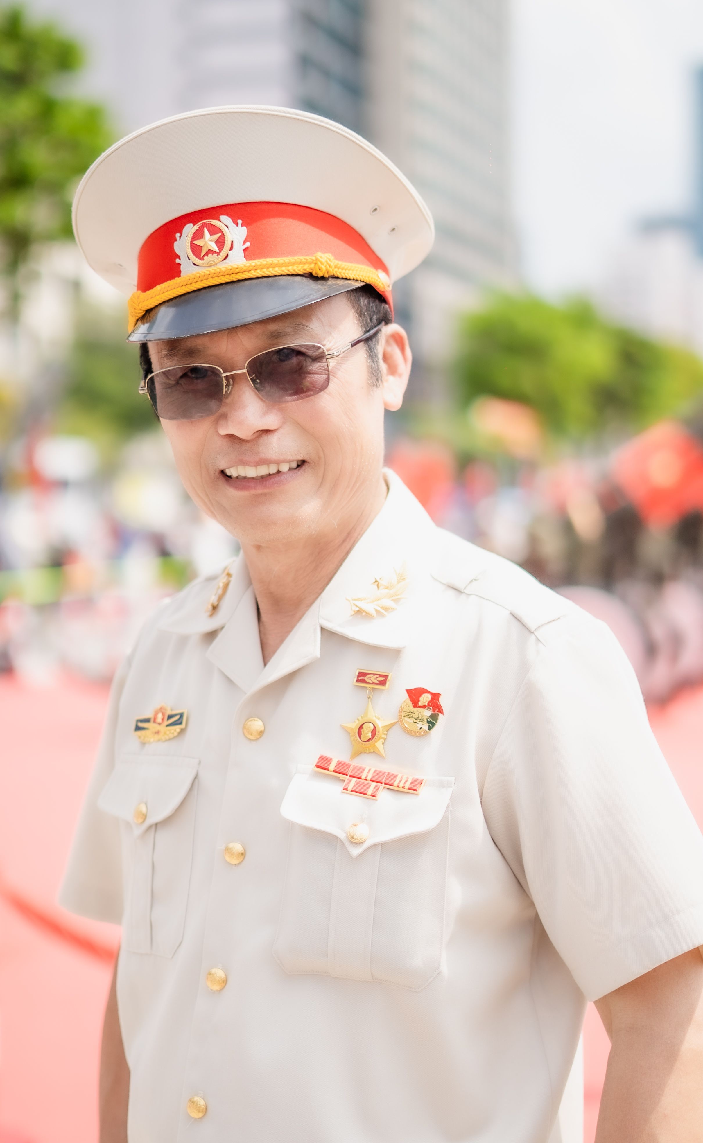 A military officer in white uniform smiling during a parade with fellow officers in the background.