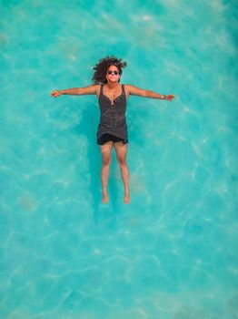 A woman relaxes while floating on her back in a clear blue swimming pool, enjoying a sunny day.