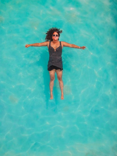 Free A woman relaxes while floating on her back in a clear blue swimming pool, enjoying a sunny day. Stock Photo