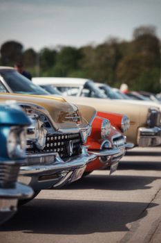 Colorful vintage cars lined up in perfect alignment at an outdoor car show under a clear sky.