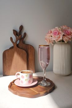 A stylish arrangement of a coffee cup, glass, and flowers in soft natural light, creating a cozy feel.