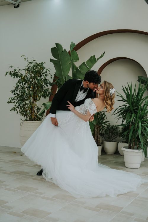 Free A bride and groom share a romantic kiss indoors among lush green plants. Stock Photo