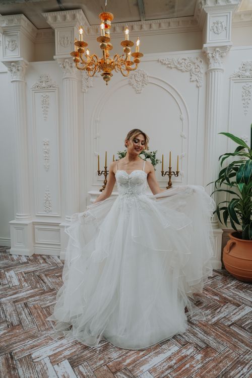 Free Bride in elegant gown posing indoors with luxurious decor and chandelier. Stock Photo