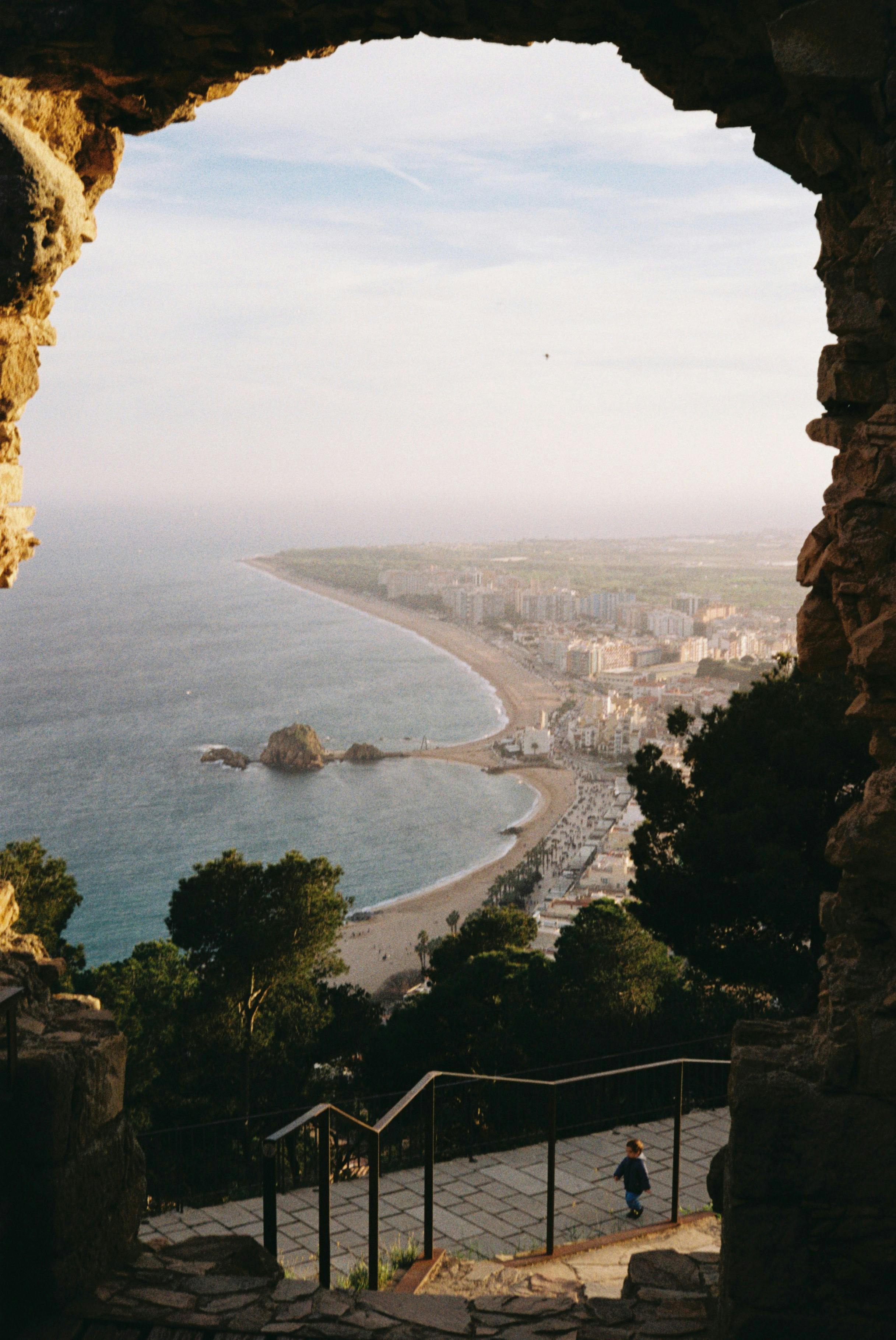 Captivating view of Blanes coastline through historic castle ruins, featuring sandy beaches and Mediterranean Sea.