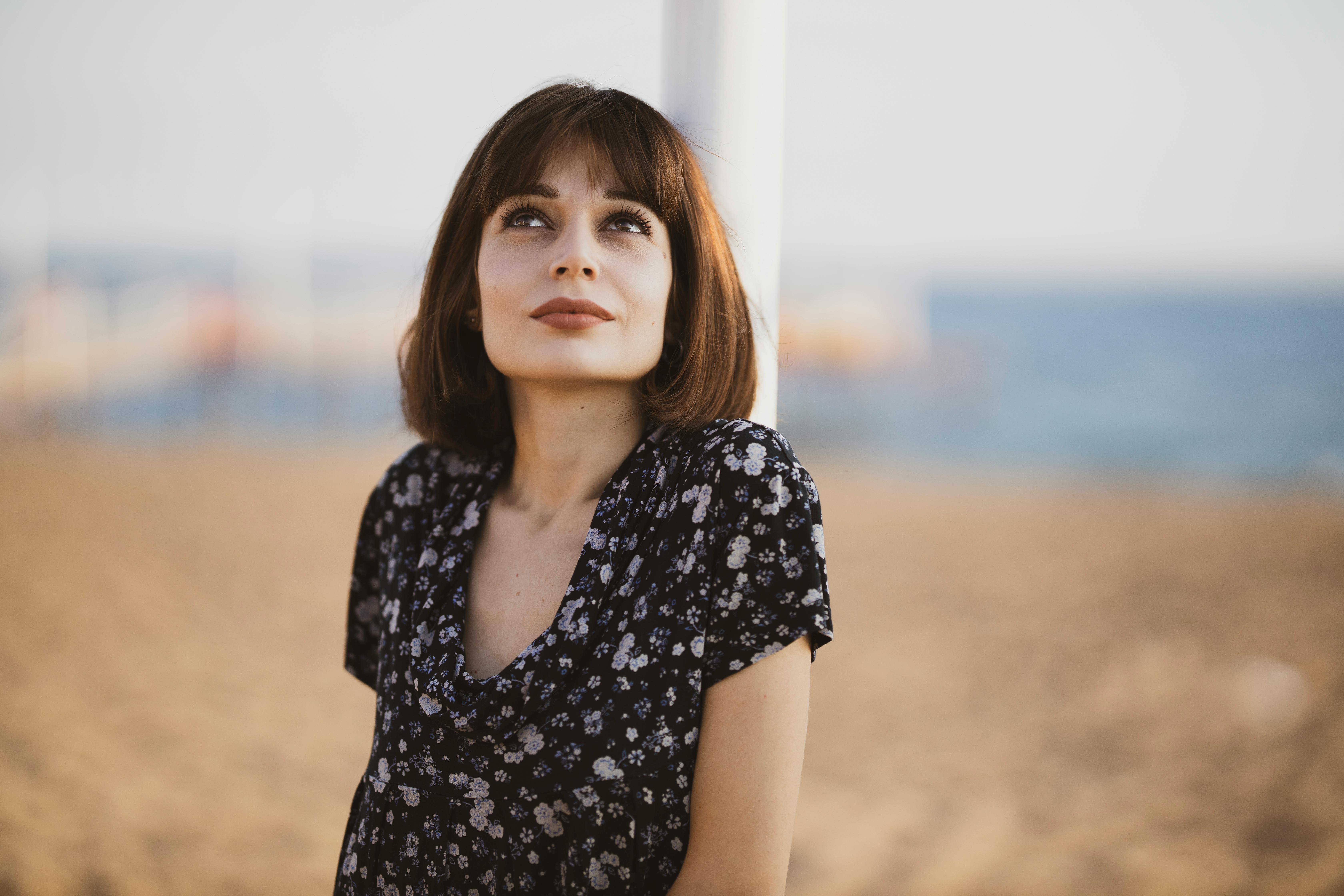 海滩边，一位穿着花卉连衣裙的年轻女子若有所思地抬头仰望