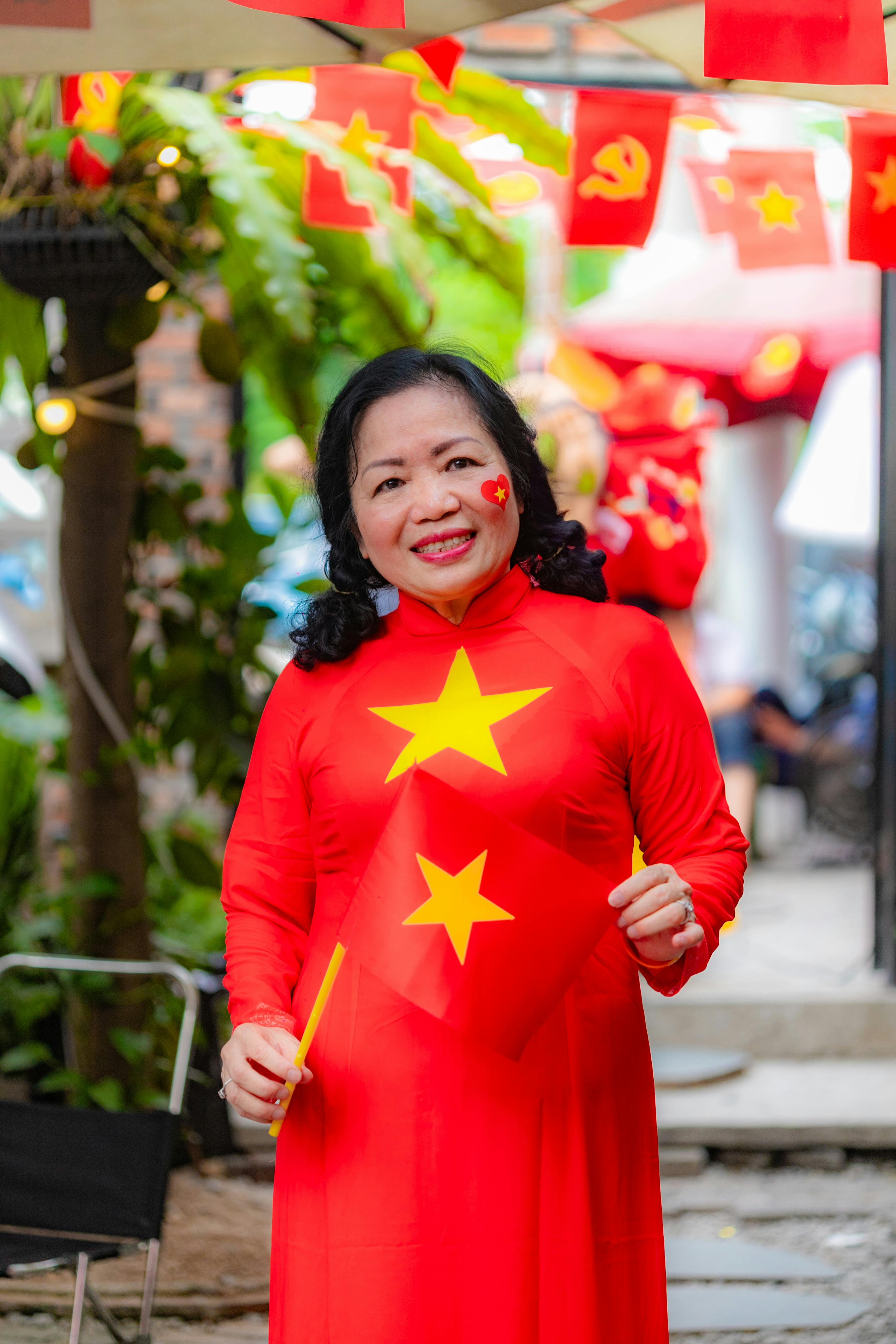 Smiling woman in red Áo dài holding Vietnam flag during a celebration.