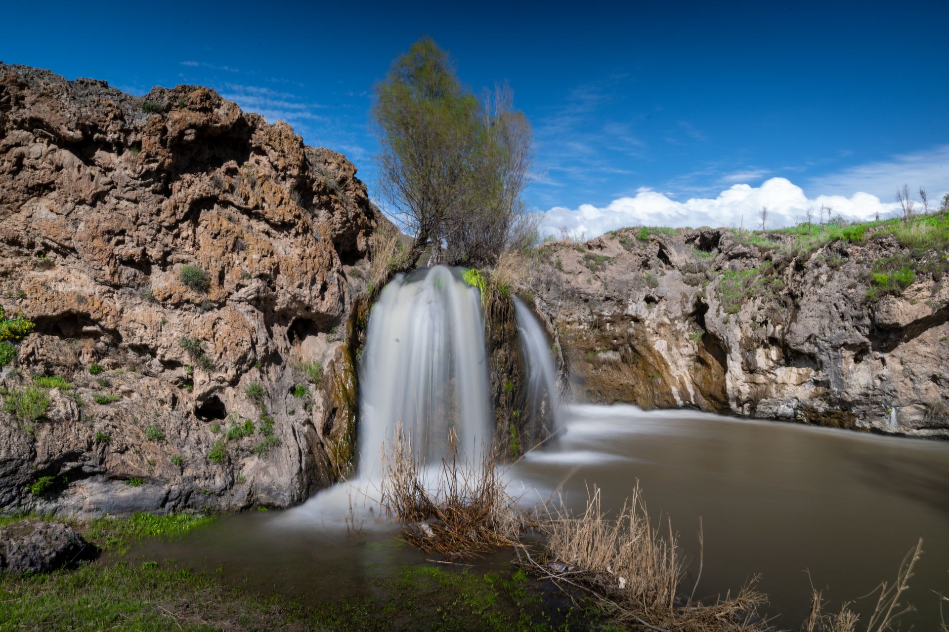 Stunning waterfall flowing over rocky cliffs surrounded by lush spring vegetation.