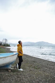 A man in a yellow jacket stands by a serene lake, enjoying the tranquil scenery.