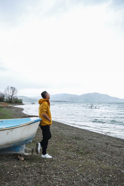 A man in a yellow jacket stands by a serene lake, enjoying the tranquil scenery.