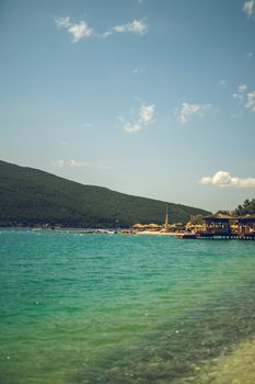 Serene beach scene with turquoise waters and distant mountains under a clear sky.