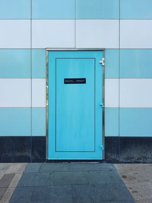 A bright blue door set in a modern, minimalist tiled wall provides a vivid contrast and architectural interest.