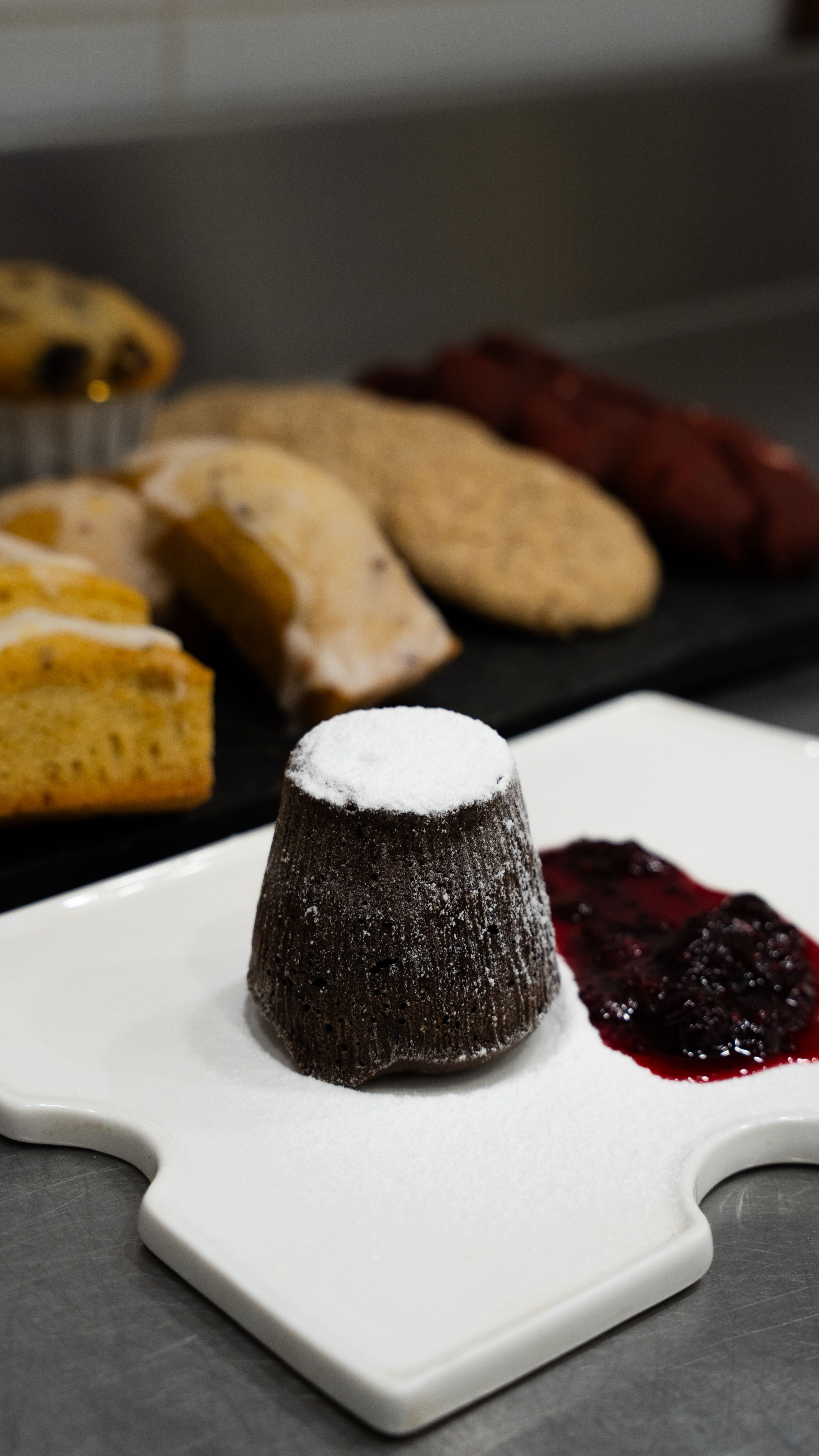 Assorted desserts including chocolate lava cake and fruit compote, presented on a white plate in a kitchen setting.