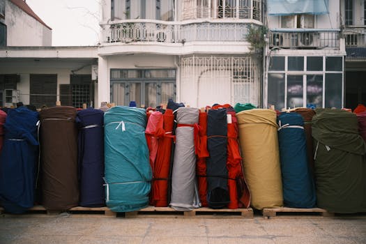 Vibrant rolls of fabric arranged outside an old building, creating a colorful display. Ideal for textile and design themes.