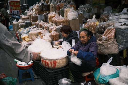 Two women working at an outdoor market stall filled with nuts and spices.