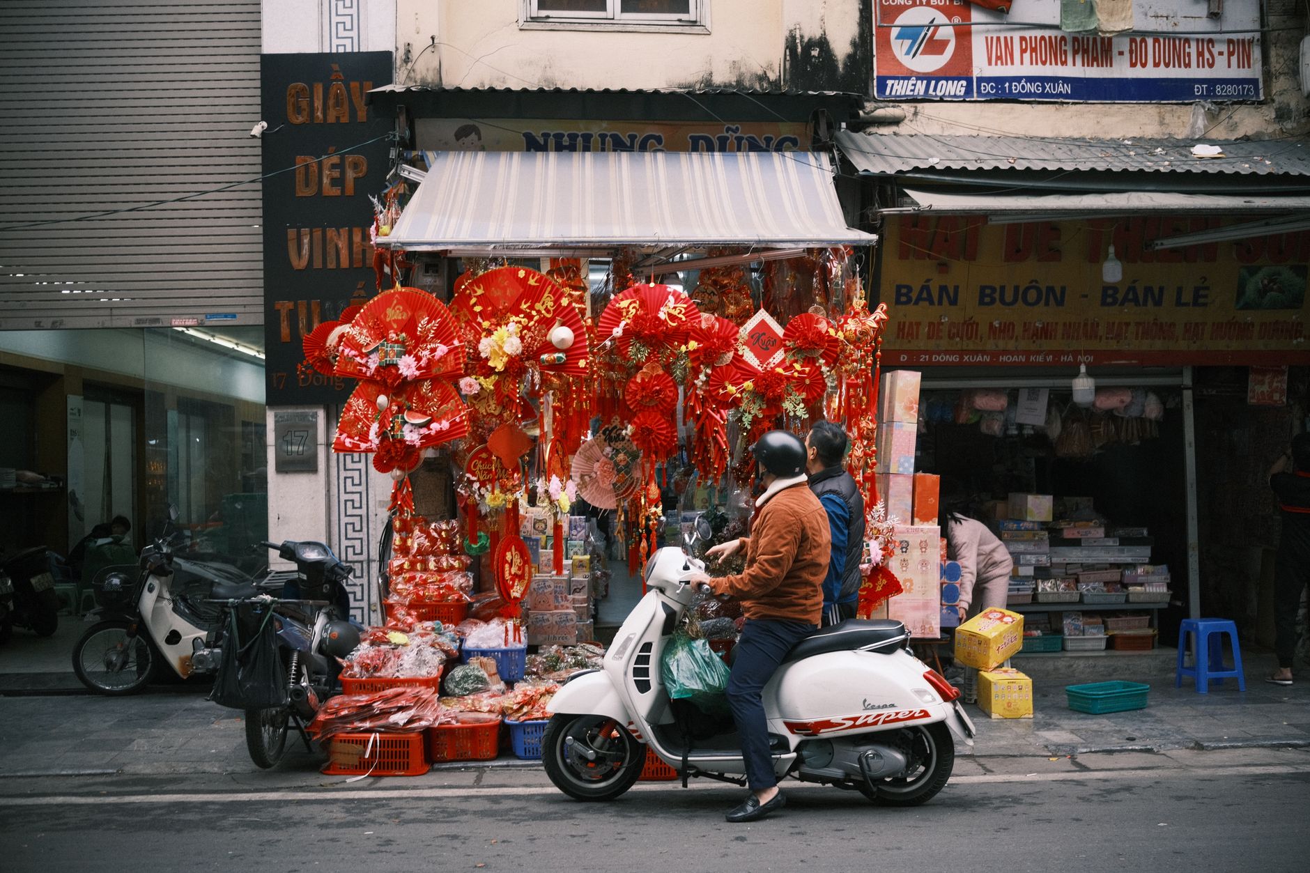Two people on a scooter passing by a vibrant street market in Vietnam adorned with red festive decorations.