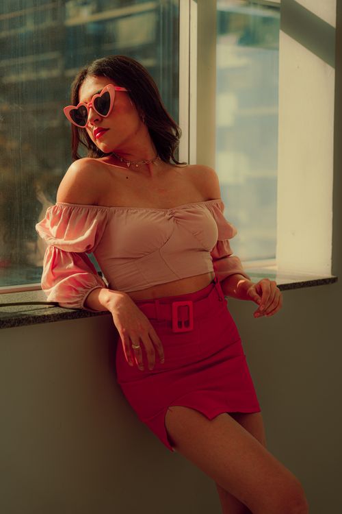 Free Trendy woman with pink sunglasses and outfit poses indoors by a sunny window. Stock Photo