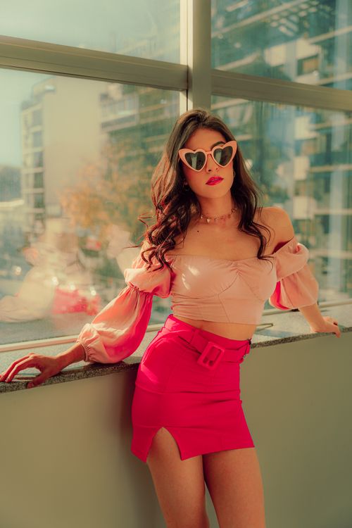 Free Fashionable woman in pink ensemble with heart-shaped sunglasses by a bright window, exuding confidence. Stock Photo